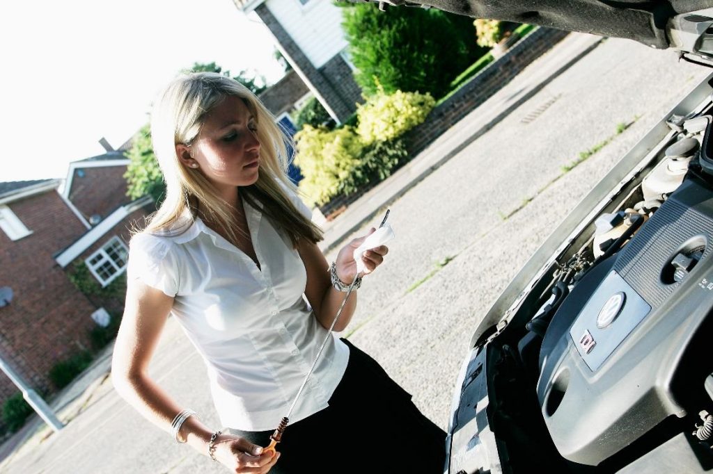 how much oil does my car need. image of woman checking a dipstick under a car's open bonnet