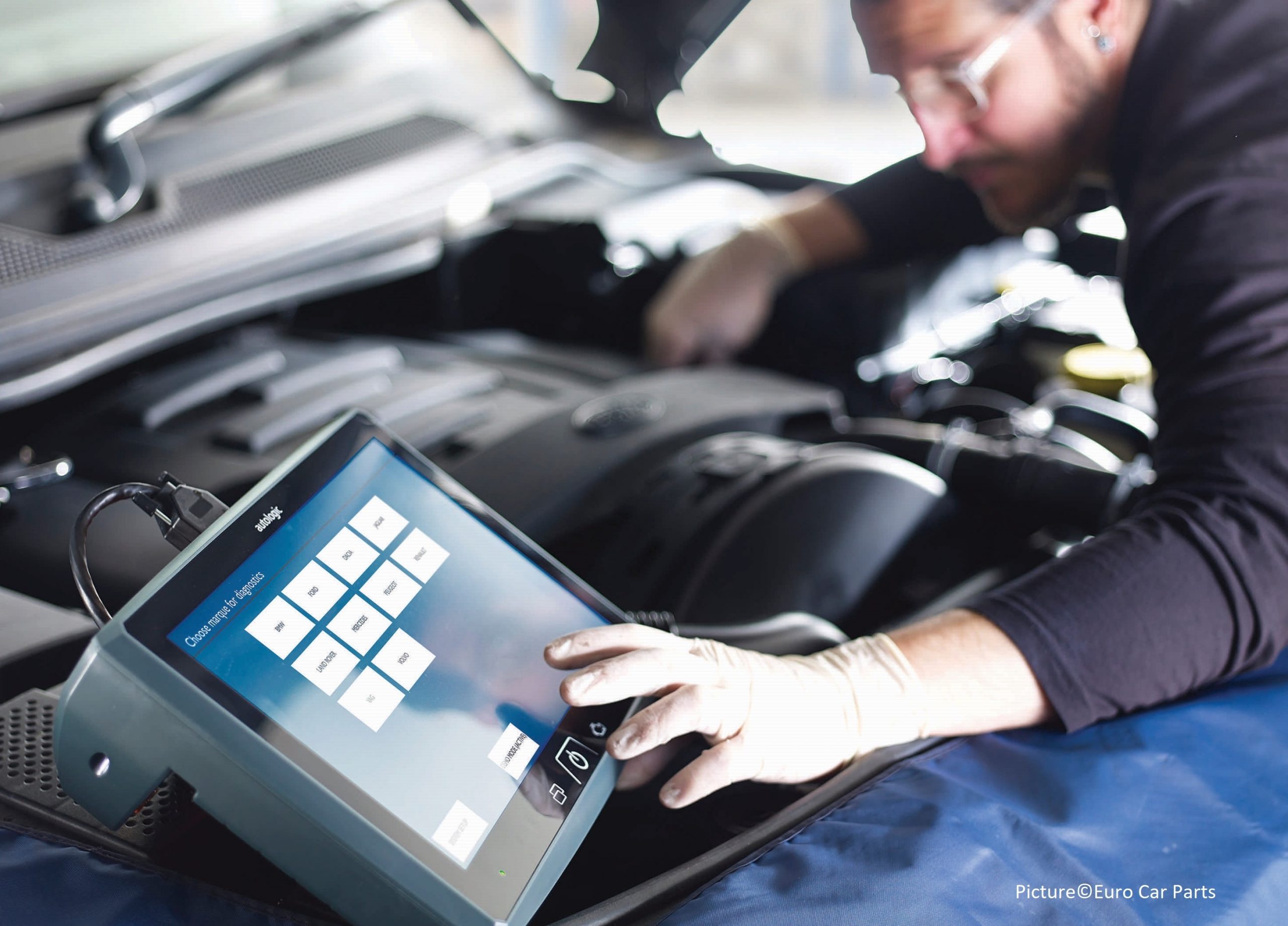 mechanic looks at diagnostic computer while under a car's bonnet inspecting the engine