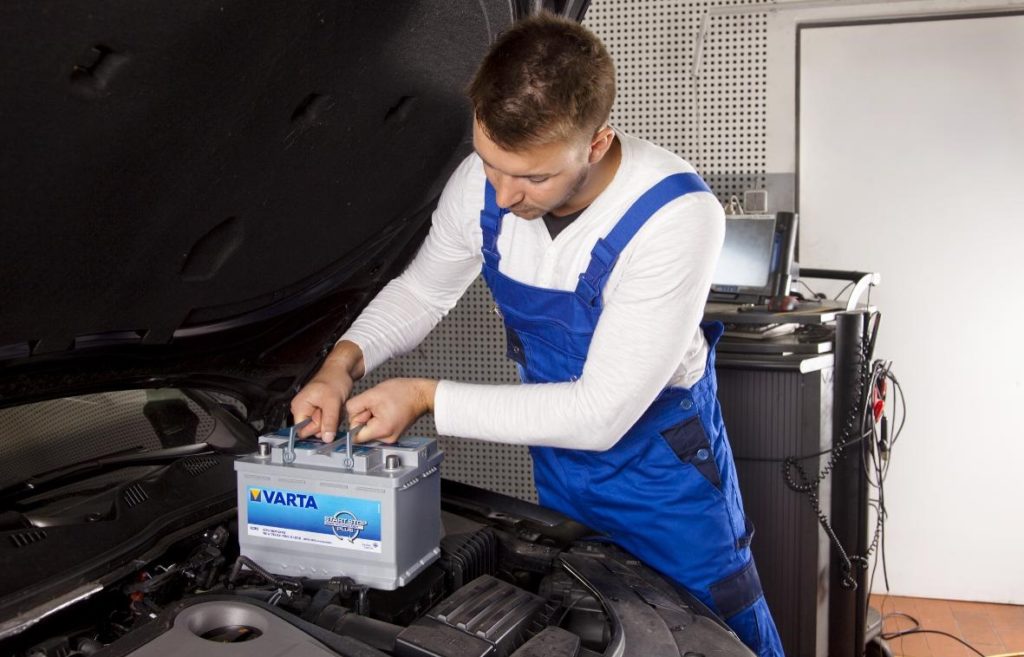 store a car. image of mechanic in blue overalls changing a car battery