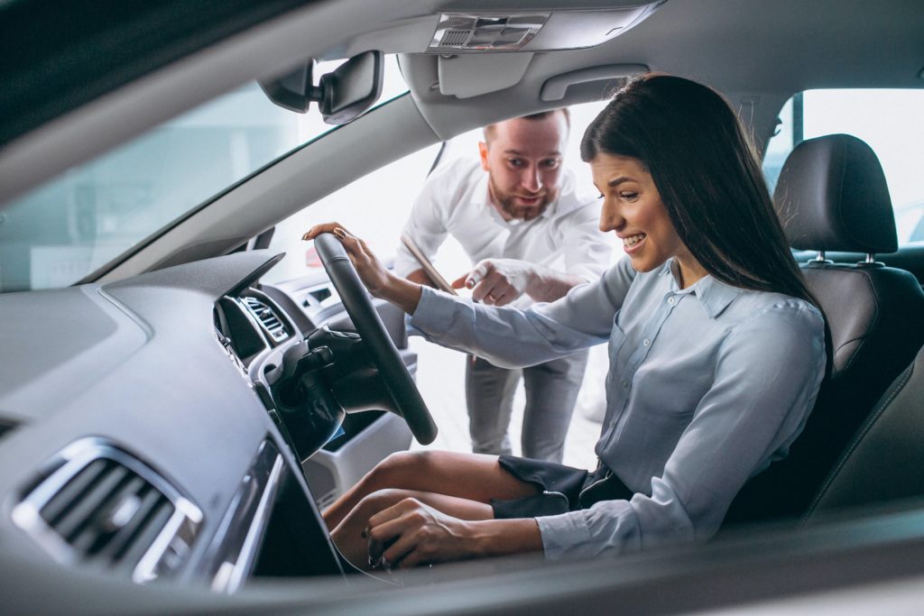 woman sitting in a car looking pleased as a salesman explains things to her