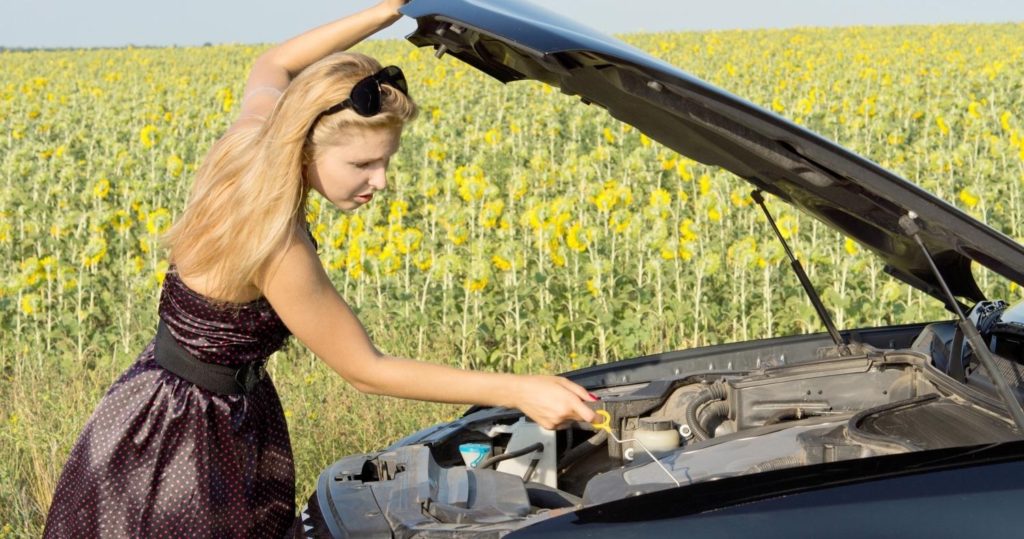 image of girl in brown dress pulling out a dipstick from under a car's open bonnet